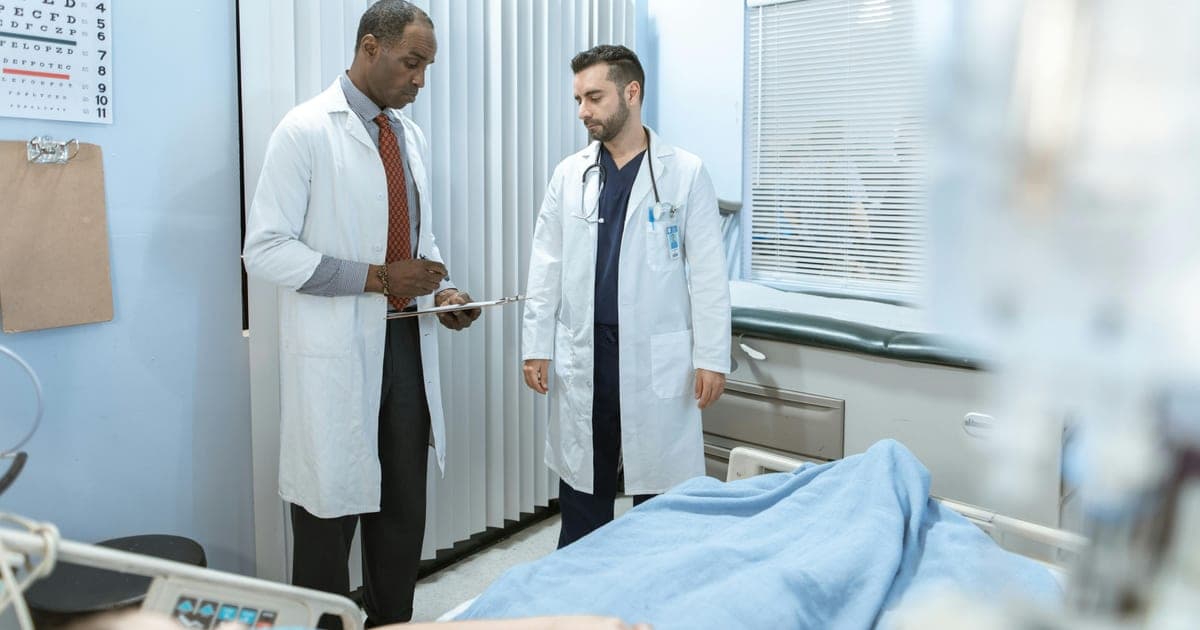 Two doctors discussing care beside a hospital bed.